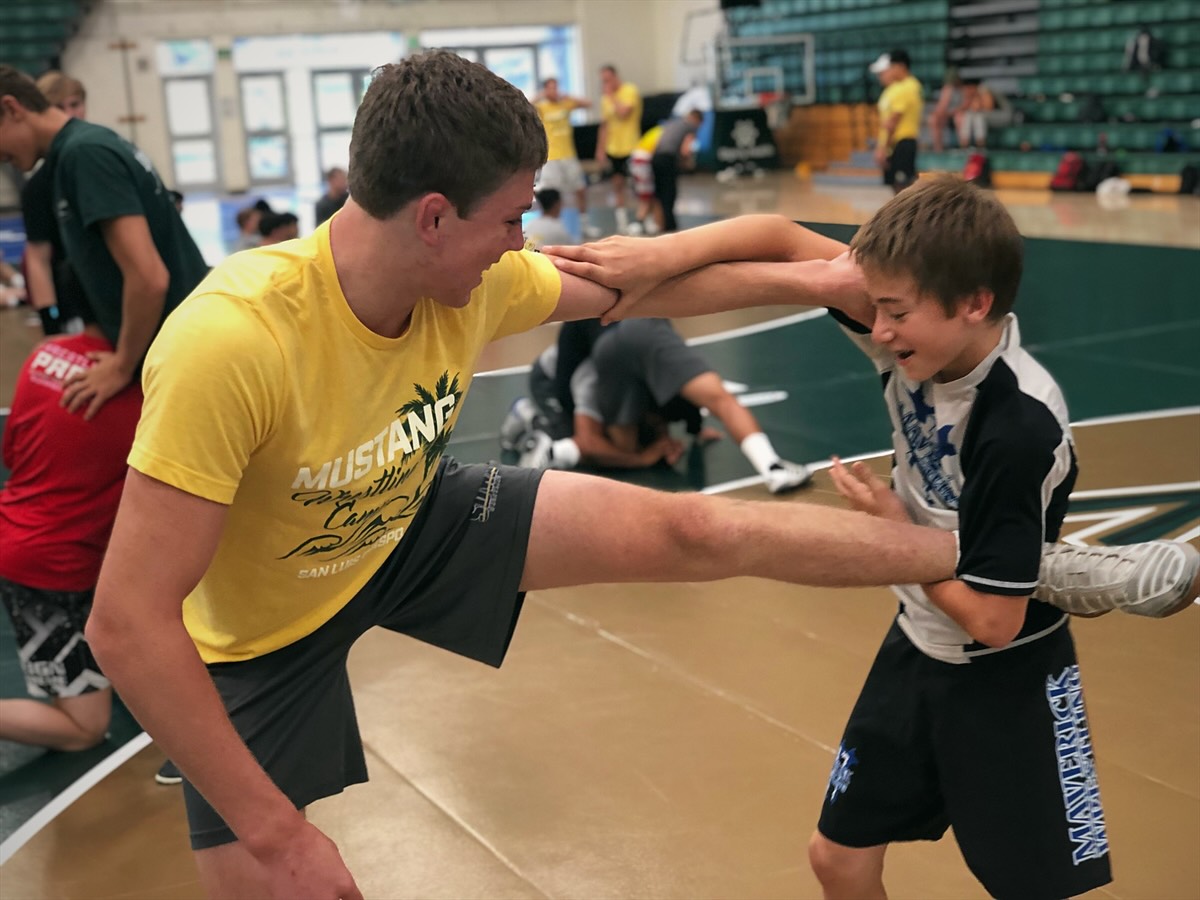 A camp staff member and a young camper laughing while they drill a leg attack